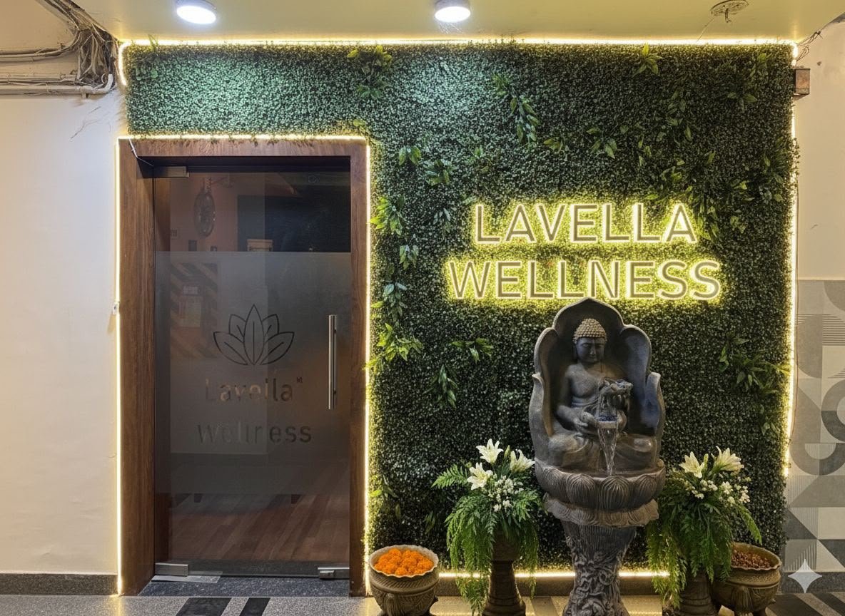 Lavella Wellness entrance — neon sign on living moss wall framed in warm LEDs, Buddha fountain and white lily offerings